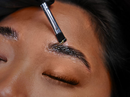 24 karat gold Plump being applied with a silicone brush on a model at the end of a brow lamination service