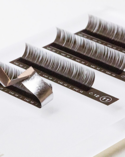 Tweezers peeling up a strip of Brunette Lash extensions.