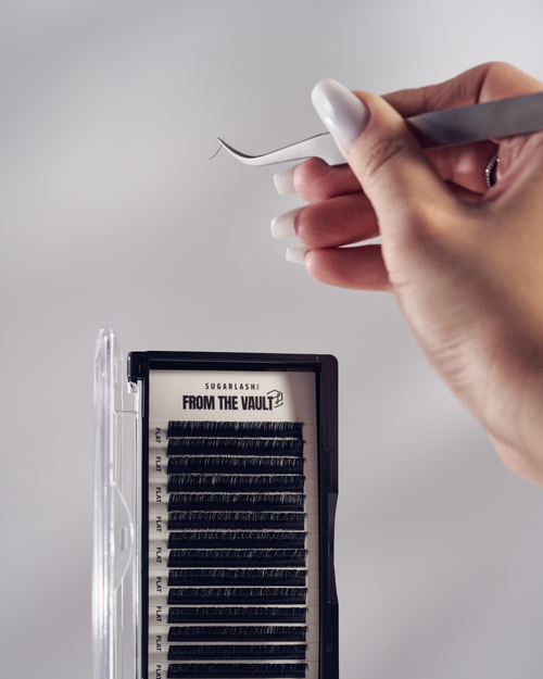 A model holding a pair of tweezers above a tray of From The Vault Flat Lashes.