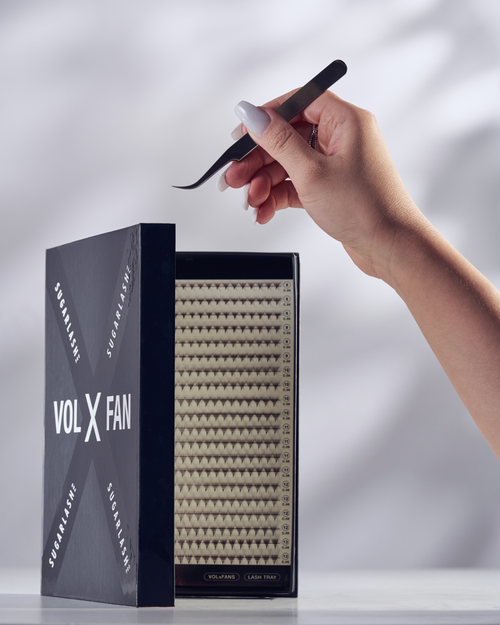 A model holding tweezers over an open tray of VOL-X Pre-made fans for volume eyelash extensions.
