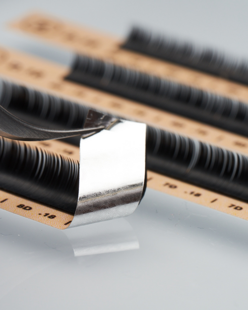 Tweezers peeling up a row of Flat lashes for eyelash extensions.