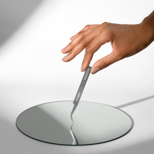 Model holding Universal Tweezer U-Curve for lash extensions against a mirror.