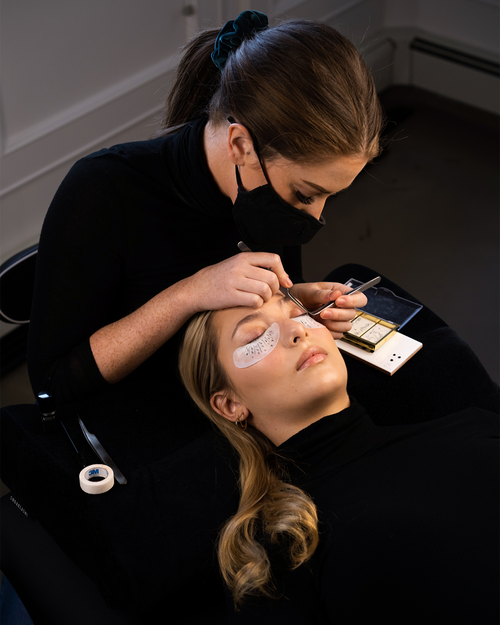 Wearing a Facemask while Applying Eyelash Extensions to a model.