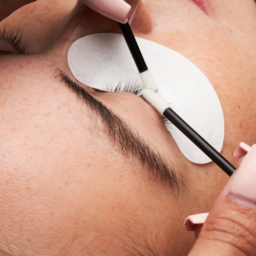 A lash artist prepping a client's lash extensions using two Flocked Applicators.