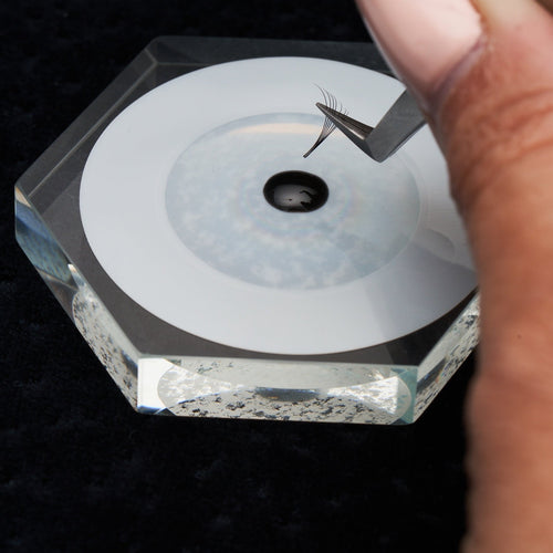 Tweezers holding a volume lash extensions fan and dipping it into lash adhesive.