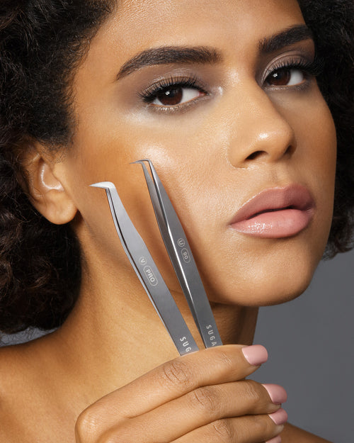 A model holding two lash Tweezers up near her cheek.
