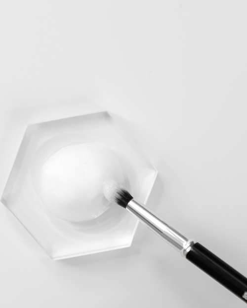 A Lash Brush dipping into a small tile holding foaming cleanser.